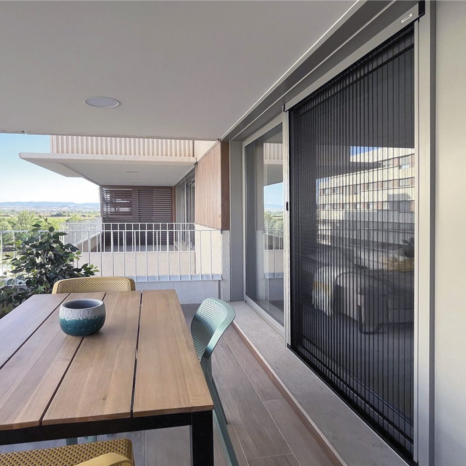 Terraza con mesa de madera y puerta corredera con mosquitera plisada negra cerrada